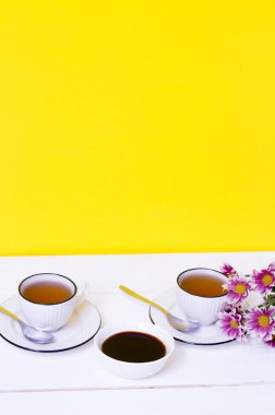 Beyaz ahşap bir masada iki fincan çay ve pekmez ve sarı bir arka plan. Kahvaltıda. Pembe harezantemlar. Üzüm suyu, keçiboynuzu pekmez, Türk tatlılığı. 