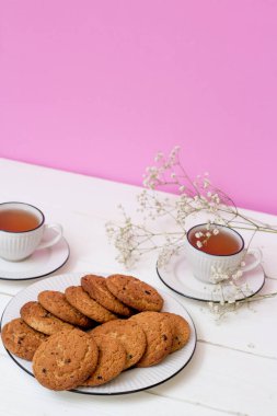 Beyaz ahşap masa ve pembe arka planda iki fincan çay ve yulaf ezmeli kurabiye. Kahvaltı.. 