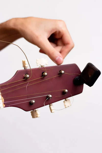 Gitar akortçusu. Beyaz arka planda tahta gitar. Gitar akordu. Adam gitarı akort ediyor.