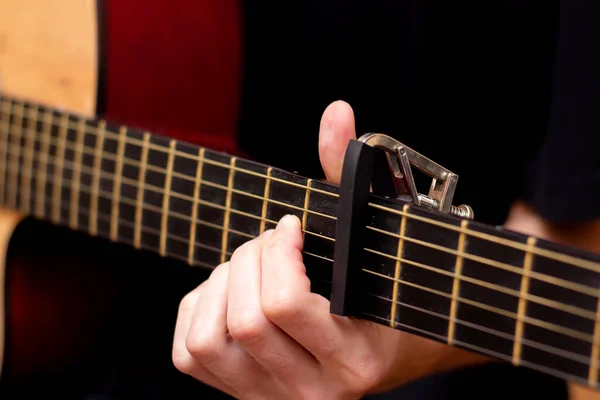 The guy plays the guitar. Capo on the guitar fretboard. Close plan. Wooden guitar.