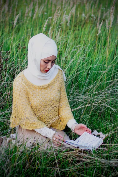 A Muslim woman in the field reads the holy book of the Koran. Muslim rosary. Muslim woman in beige hijab. Beauty, femininity, tenderness.