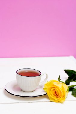 Bir fincan çay ve yulaflı kurabiye. Sarı gül. Kahvaltıda. Çay içiyorum. Beyaz ahşap zemin ve pembe duvar.