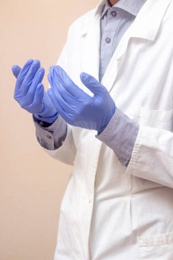 Beyaz paltolu genç bir adam ellerini kaldırdı ve dua etti. Tıbbi eldivenler. Bej arka plan. Doktor dua ediyor. Bir Müslüman dua eder.