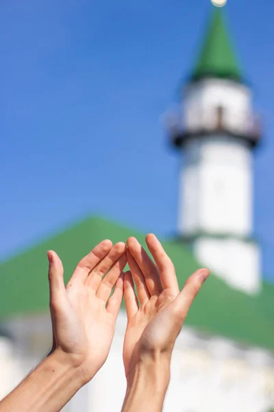 Hands raised in prayer. Muslim man praying on the background of the mosque.