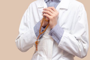 Beyaz cüppeli genç bir adam ellerini kaldırdı ve Müslüman bir tespihle dua etti. Bej arka plan. Doktor dua ediyor. Bir Müslüman dua eder..