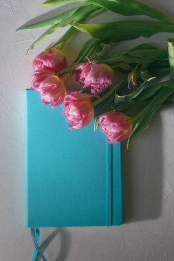 Beyaz zemin üzerinde laleler olan mavi defter.