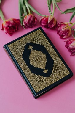 Pembe arka planda çiçekli kutsal Kur 'an. Laleler. Ramazan. Kuran 'ın Hatm' ı. Kuran okuyarak. Ramazan konsepti. İslam kavramı.