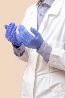 Beyaz paltolu genç bir adam ellerini kaldırdı ve dua etti. Tıbbi eldivenler. Bej arka plan. Doktor dua ediyor. Bir Müslüman dua eder.