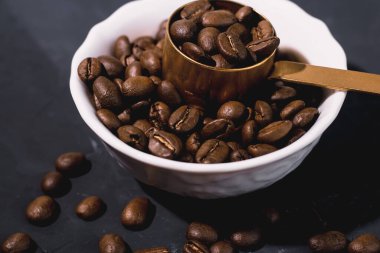 Siyah arka planda beyaz tabakta kahve çekirdekleri. Kahve çekirdekleri için demir kaşık