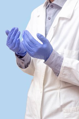 Beyaz paltolu genç bir adam ellerini kaldırdı ve dua etti. Tıbbi eldivenler. Mavi arka plan. Doktor dua ediyor. Bir Müslüman dua eder.