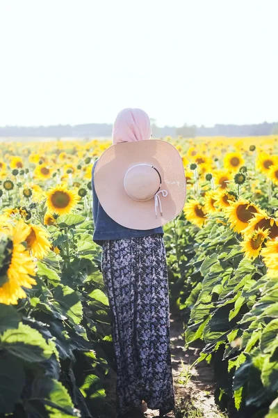 Muslim woman with hat on the field with sunflowers. Yellow sunflowers. Full length.