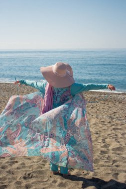Deniz kıyısında mavi burkinili Müslüman bir kadın. Hasır şapka. Kutsal dinlenme. Müslüman kadın gezgin. Pareo.