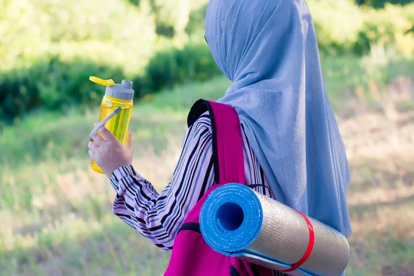 水のための黄色のボトルと森の中でバックパックとハイキングマットを持つイスラム教徒の女性 森の中でハイキング 旅行だ ピンクバックパック — ストック写真