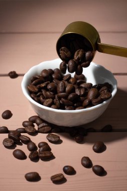 Ahşap arka planda beyaz tabakta kahve çekirdekleri. Kahve çekirdekleri için demir kaşık. Kahve içeriği, kahve dükkanı..