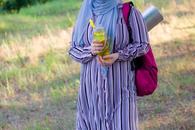 Sırt çantalı Müslüman bir kadın ve su için sarı bir şişeyle ormanda yürüyüş paspası. Ormanda yürüyüş. Seyahat. Pembe sırt çantası..