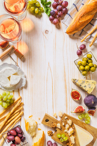 Different kinds of cheeses, wine, baguettes and fruits on white