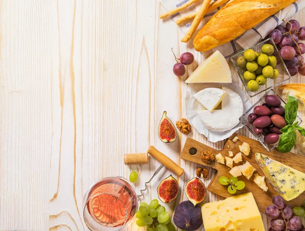 Diversi tipi di formaggi, vino e snack sul legno bianco — Foto Stock