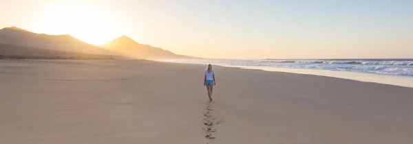 모래 사장에 발자국을 남겨두고 일몰에 걷는 여자. — 스톡 사진