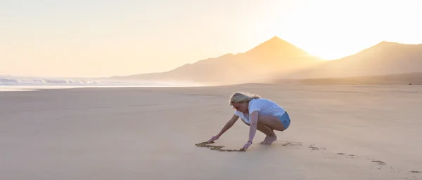 Леди рисует сердце в песке на пляже . — стоковое фото