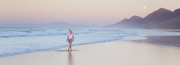 Señora caminando en la playa de arena en la puesta del sol . —  Fotos de Stock