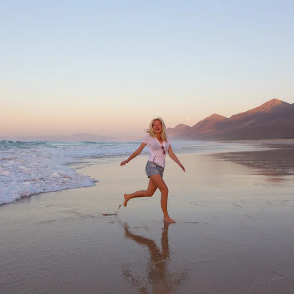 Lady enjoying running from waves on sandy beach in sunset. — Stock Photo, Image