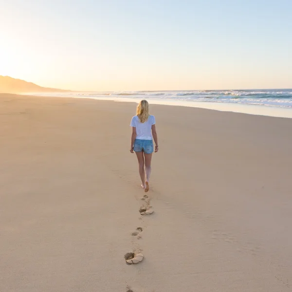 Ayak izleri geride bırakarak günbatımı kumsalda yürürken Leydi. — Stok fotoğraf