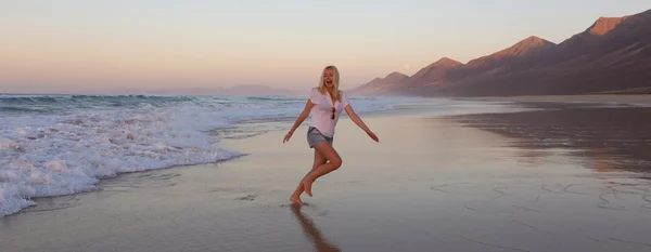 Senhora gostando de correr de ondas na praia de areia ao pôr do sol . — Fotografia de Stock