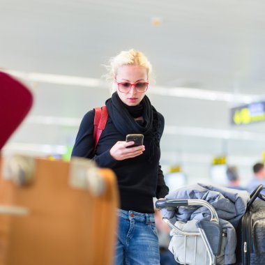 Female traveler using cell phone while waiting on airport. clipart