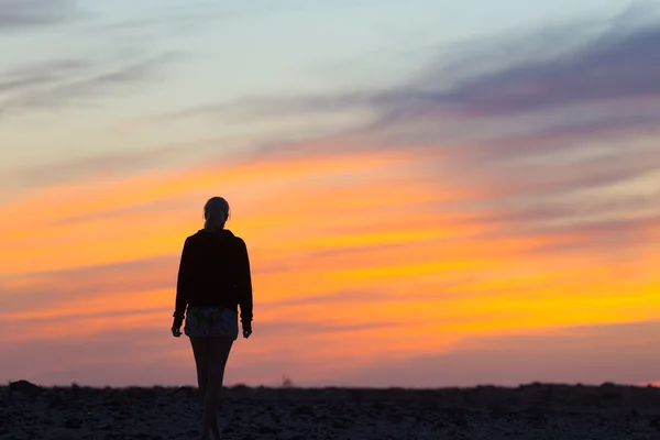 Vrouw op rotsachtige strand kijken naar zonsondergang. — Stockfoto