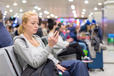 Female traveler using cell phone while waiting. clipart