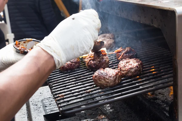 Beef burgers being grilled on food stall grill. — Stock Photo, Image