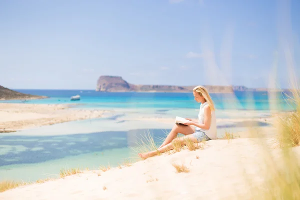 Vrouw lezen boek, genieten van de zon op het strand. — Stockfoto