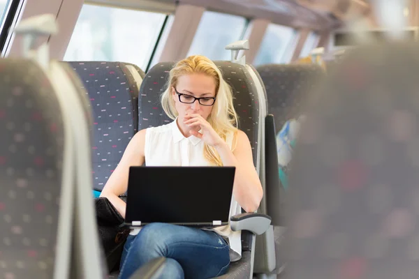 Woman travelling by train working on laptop.