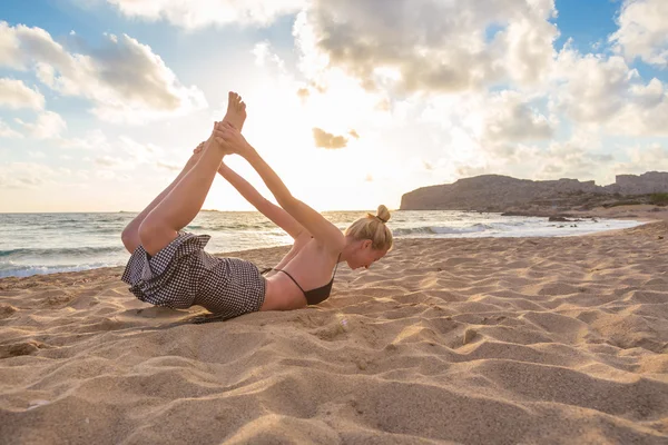 Žena cvičí jógu na mořské pláži při západu slunce. — Stock fotografie