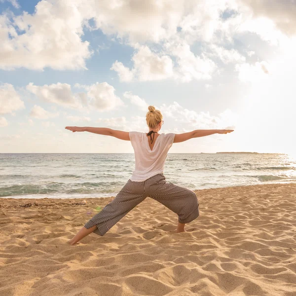 Frau praktiziert Yoga am Meeresstrand bei Sonnenuntergang. — Stockfoto