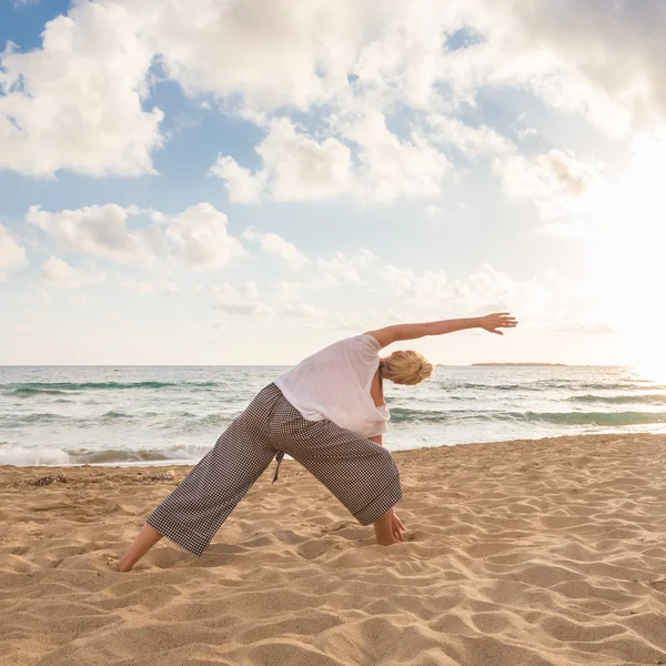 Жінка практикує йогу на морському пляжі на заході сонця . — стокове фото