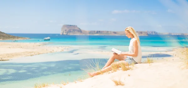 Mujer leyendo libro, disfrutando del sol en la playa . — Foto de Stock