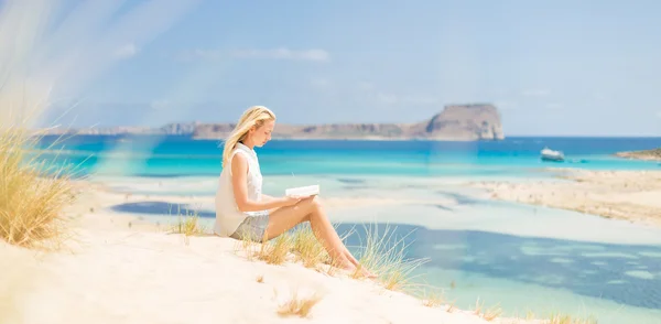 Mujer leyendo libro, disfrutando del sol en la playa . — Foto de Stock