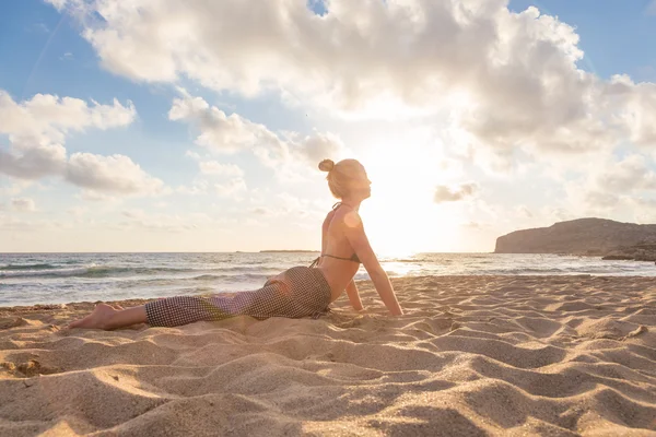 Nő gyakorolja jóga a tengerparton naplementekor. — Stock Fotó