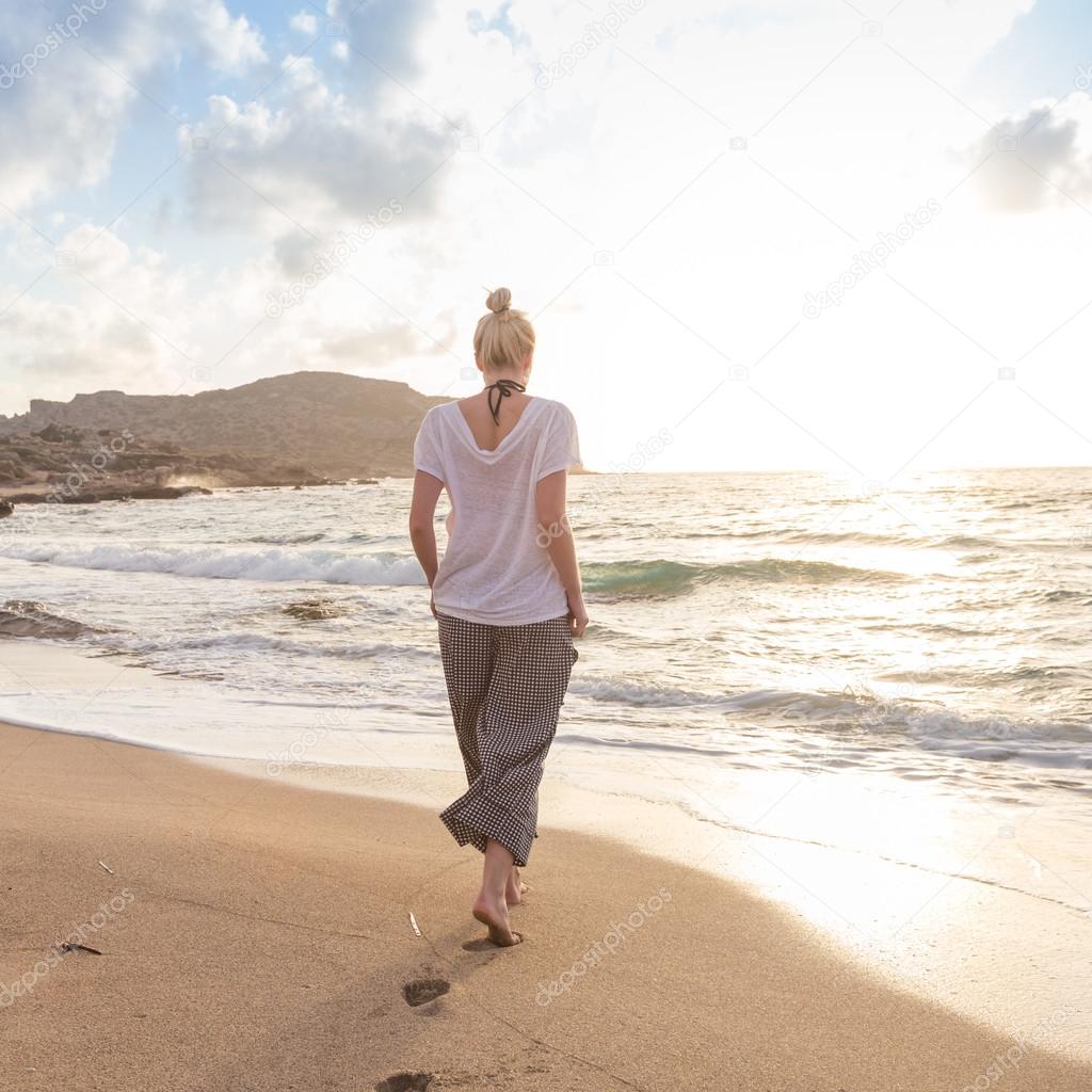 Woman walking on sand beach at golden hour