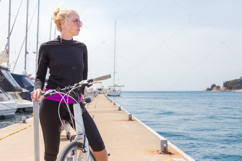 Young active woman cycling on pier in marina.