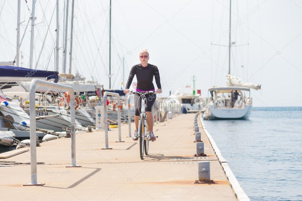 Young active woman cycling on pier in marina.