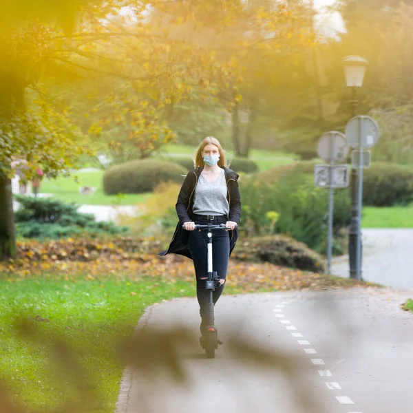 Casual caucasian teenager wearing protective face mask riding urban electric scooter in city park during covid pandemic. Urban mobility concept — Stock Photo, Image