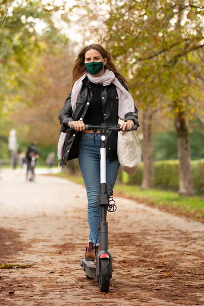 Повседневный кавказский подросток в защитной маске катается на городском электрическом скутере в городском парке во время ковидной пандемии. Концепция городской мобильности — стоковое фото