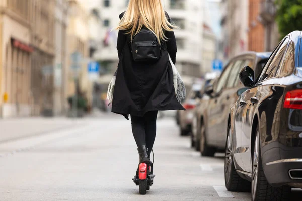 Achteraanzicht van meisje rijden openbare huur elektrische scooter in stedelijke stedelijke omgeving. Nieuw milieuvriendelijk modern openbaar stadsvervoer in Ljubljana — Stockfoto