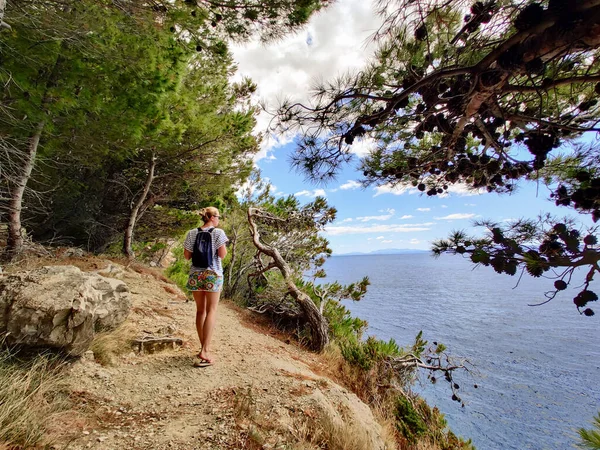 Joven turista activo con una pequeña mochila caminando por el sendero costero entre pinos que buscan una cala remota para nadar solo en paz en la costa de Croacia. Concepto de viaje y aventura — Foto de Stock