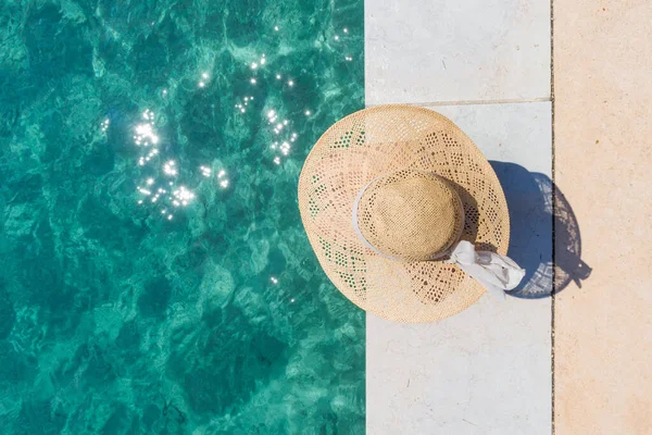 Woman wearing big summer sun hat relaxing on pier by clear turquoise sea. — Stock Photo, Image