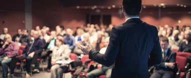 İş toplantısında konferans salonunda konuşma yapan konuşmacı. Konferans salonundaki tanınmayan seyircilerin arka görüntüsü.