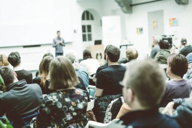 Üniversitedeki konferans salonunda sunum yapan adam.