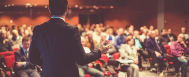 İş toplantısında konferans salonunda konuşma yapan konuşmacı. Konferans salonundaki tanınmayan seyircilerin arka görüntüsü.